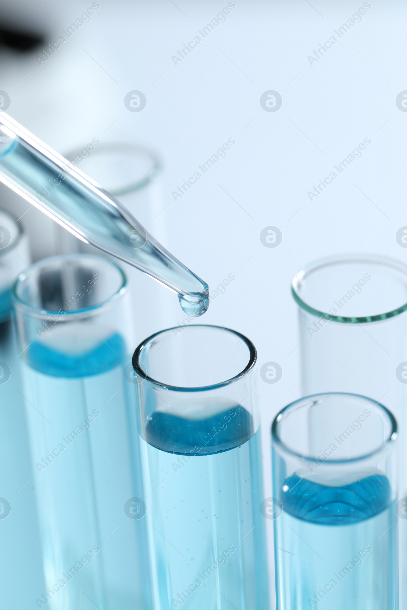 Photo of Dripping liquid from pipette into test tube on blurred background, closeup