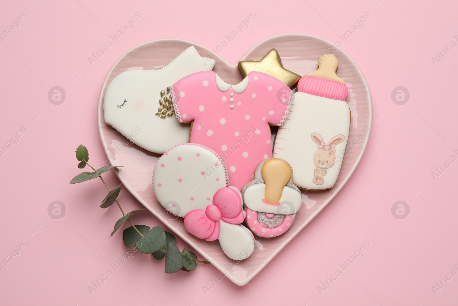 Photo of Heart shaped plate of baby shower cookies on light pink background, top view