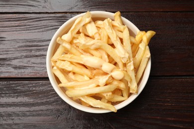 Delicious french fries with cheese sauce in bowl on wooden table, top view