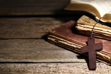 Wooden Christian cross and old books on table, closeup. Space for text