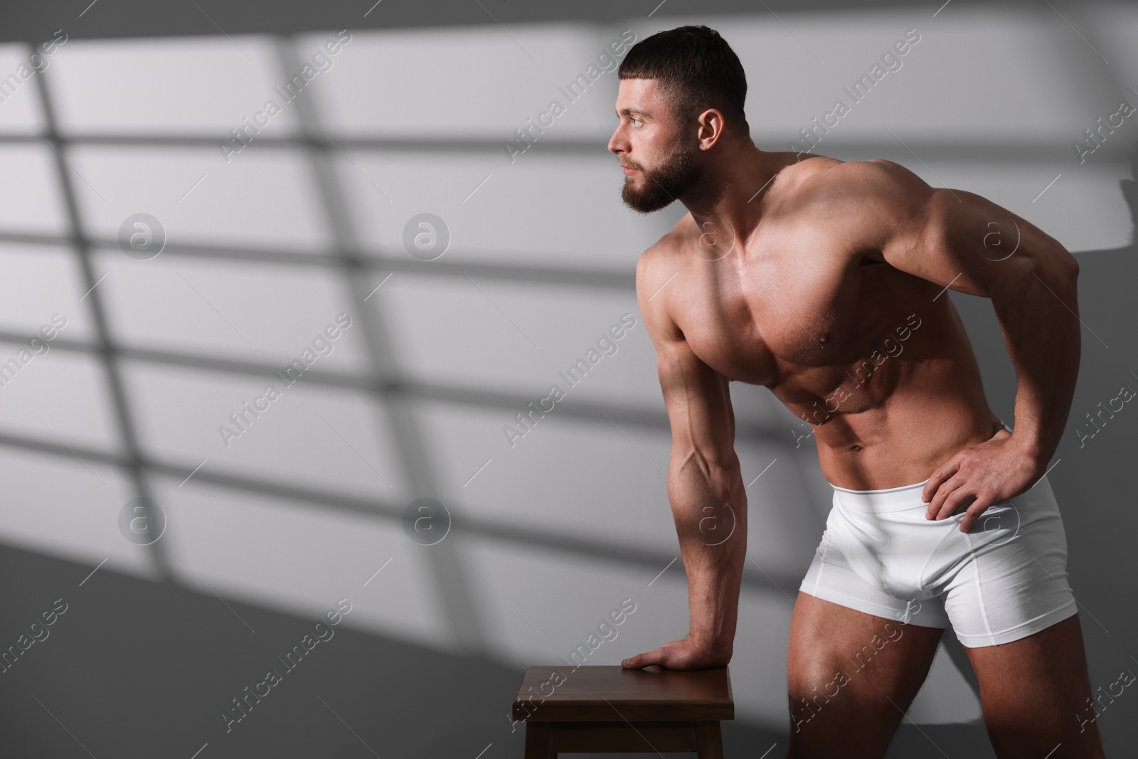 Photo of Young man in stylish white underwear near grey wall. Space for text