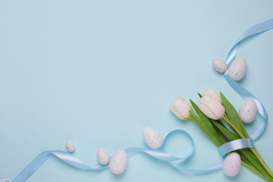 Many painted Easter eggs, tulip flowers and ribbon on light blue background, flat lay. Space for text