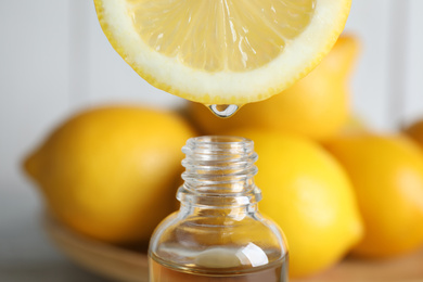 Photo of Citrus essential oil dripping from lemon slice into bottle, closeup