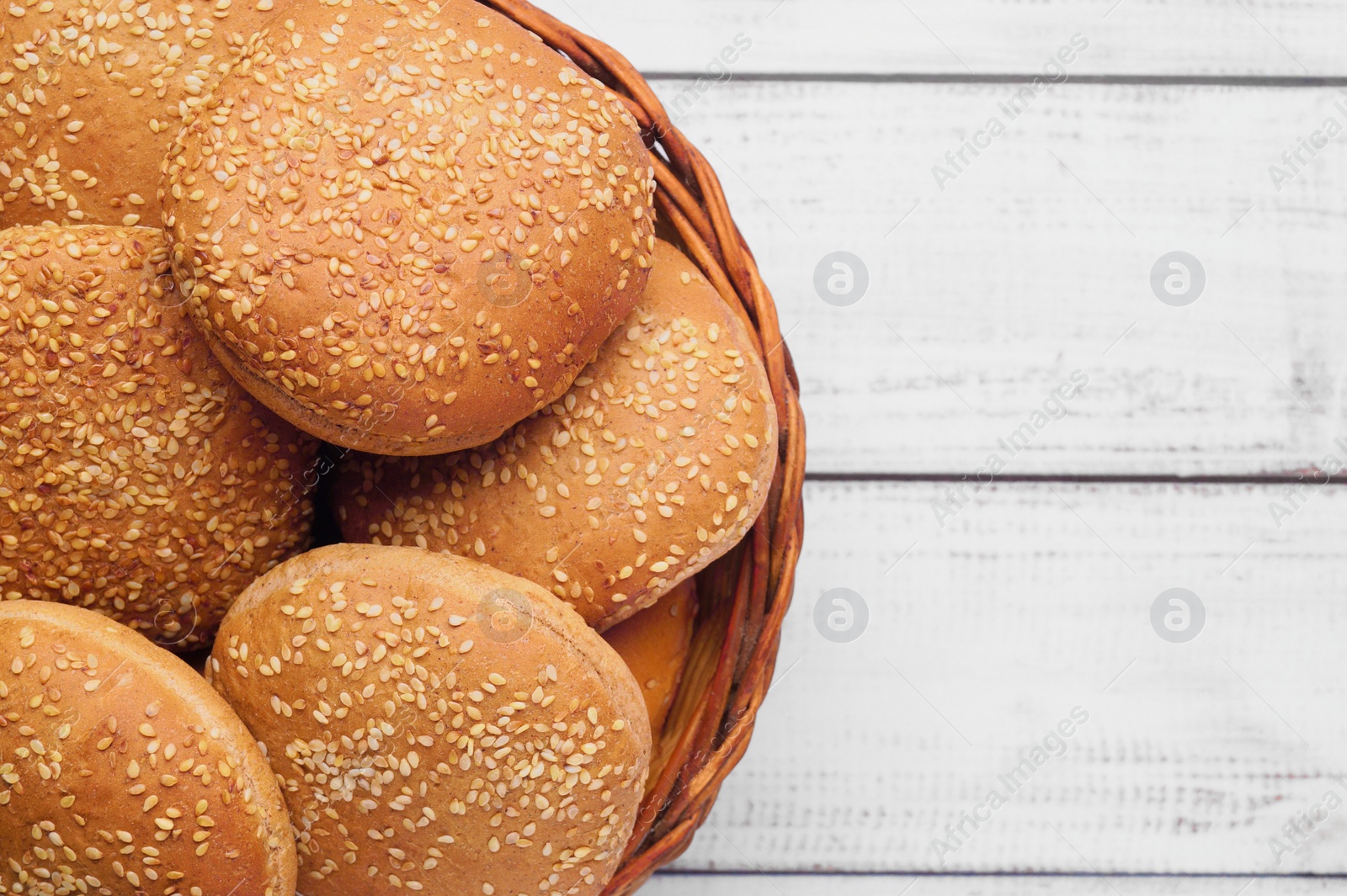 Photo of Wicker basket of fresh buns with sesame seeds on white wooden table, top view. Space for text