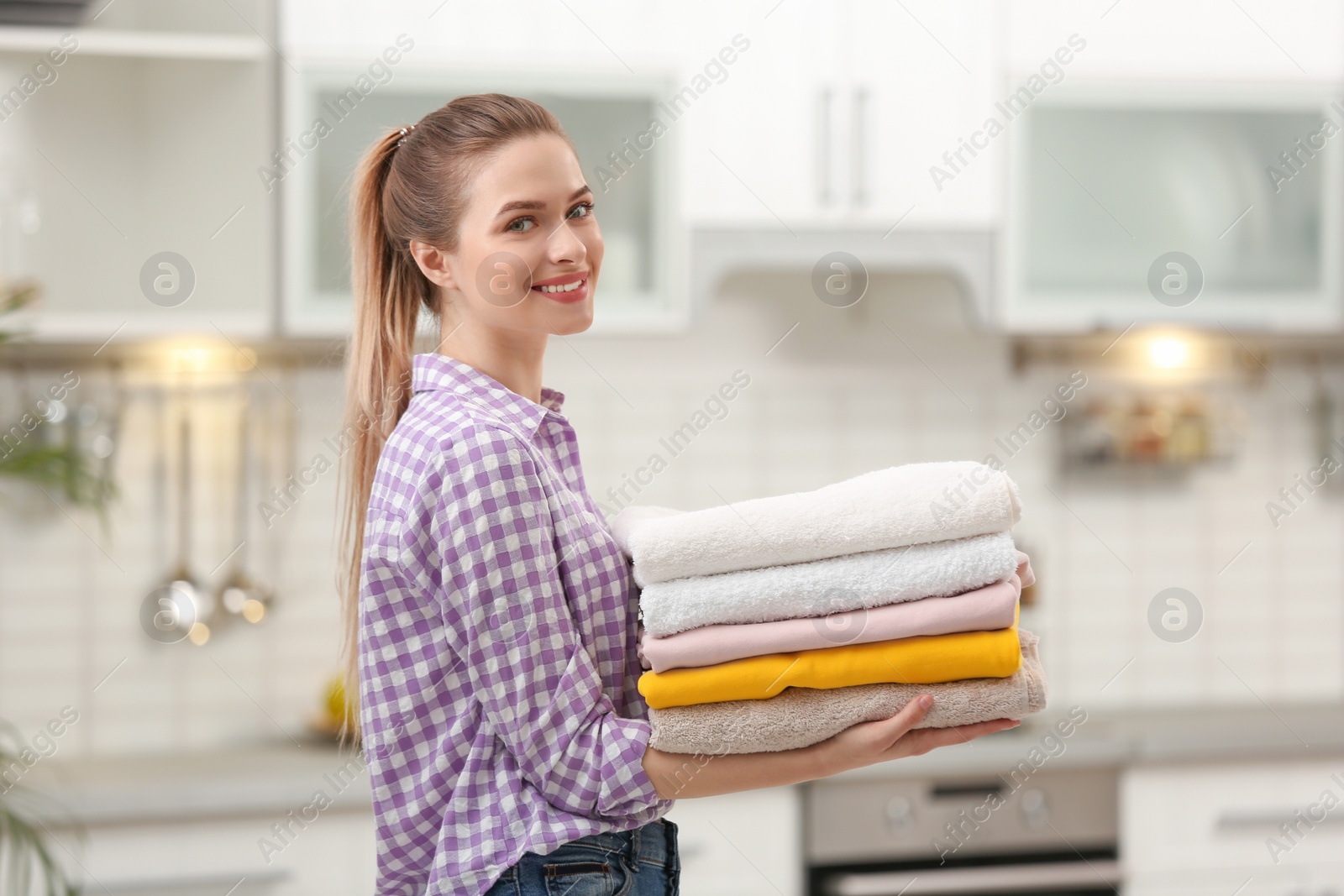 Photo of Woman holding folded clean towels in kitchen. Laundry day