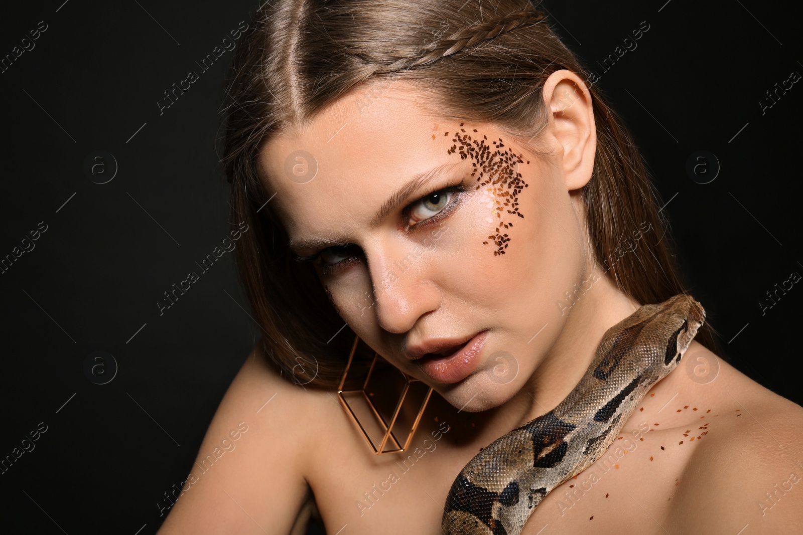 Photo of Beautiful woman with boa constrictor on black background, closeup