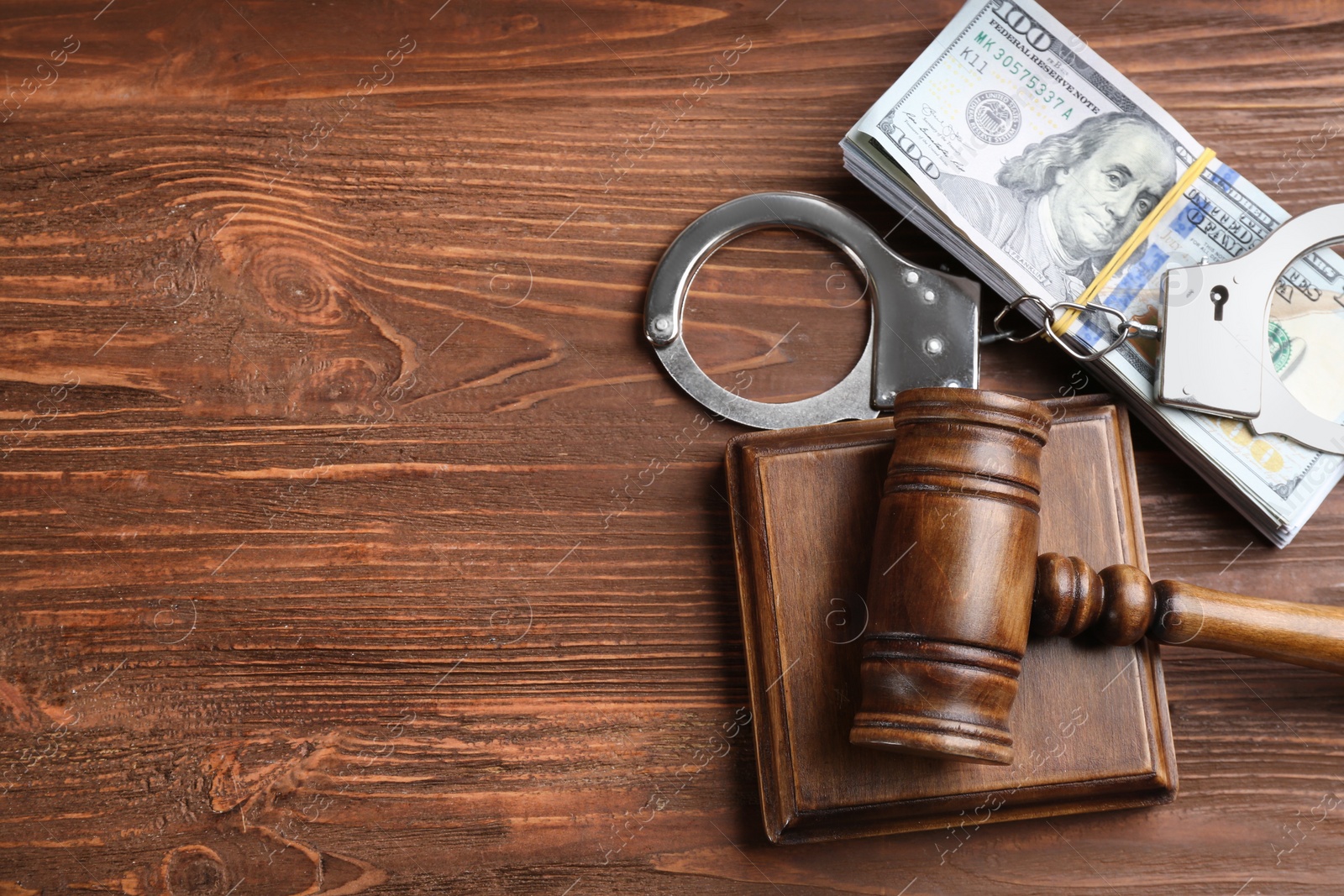 Photo of Dollar bills, gavel and handcuffs on wooden table, flat lay with space for text. Bribe concept