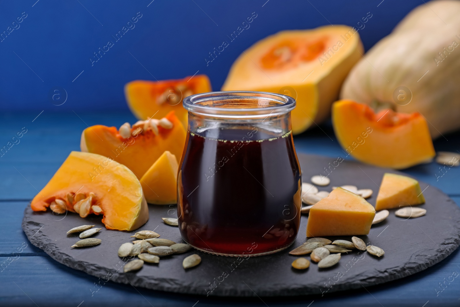 Photo of Fresh pumpkin seed oil in glass jar on blue wooden table