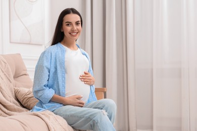 Happy pregnant woman on sofa at home, space for text