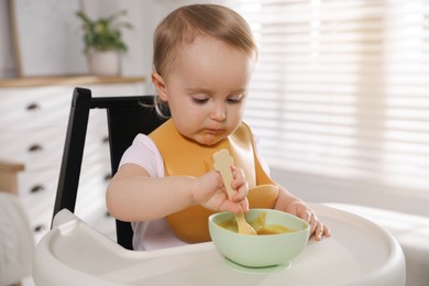 Photo of Cute little baby wearing bib while eating at home