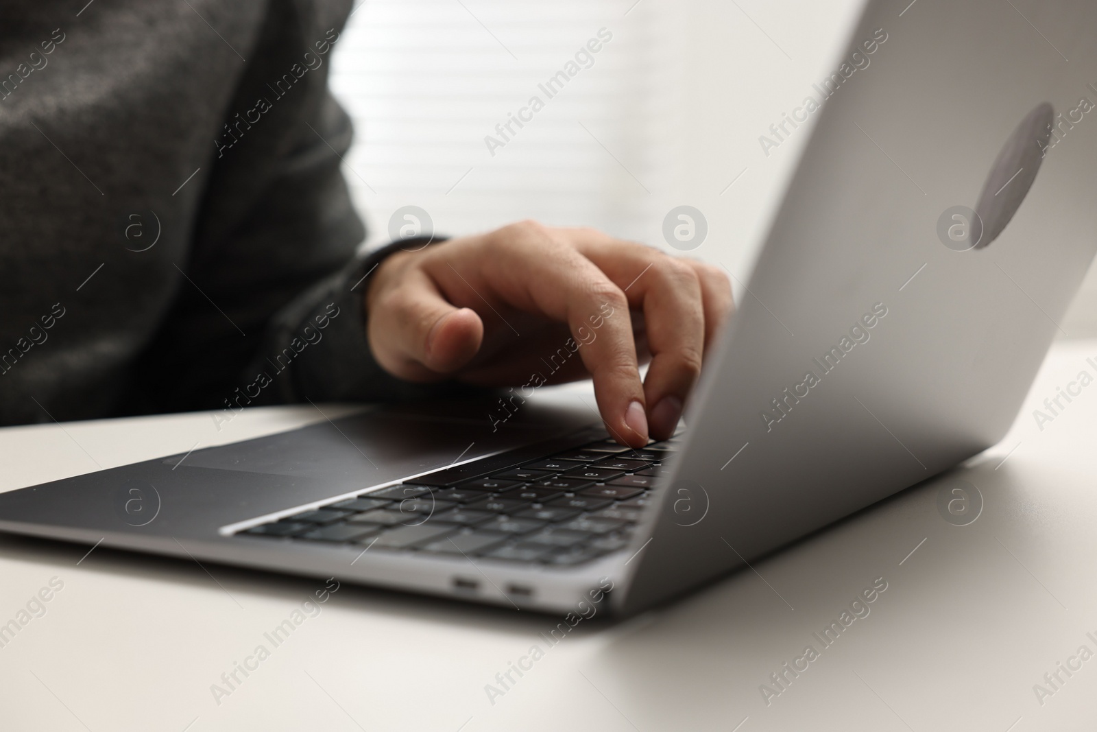 Photo of E-learning. Young man using laptop at white table, closeup