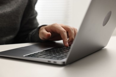 Photo of E-learning. Young man using laptop at white table, closeup