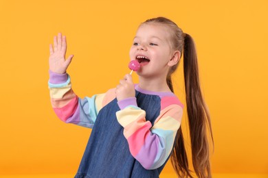 Photo of Happy little girl with lollipop on orange background