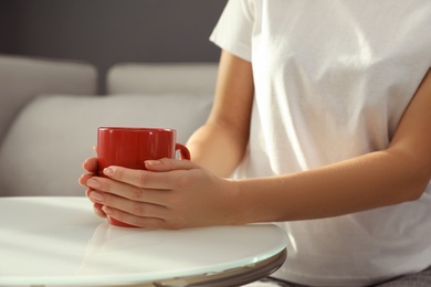 Woman with red cup at table indoors, closeup