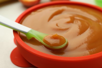 Photo of Bowl and spoon with tasty pureed baby food on white table, closeup