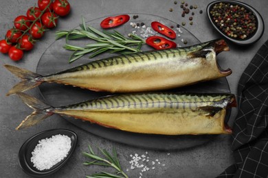 Photo of Delicious smoked mackerels and spices on dark grey table, flat lay