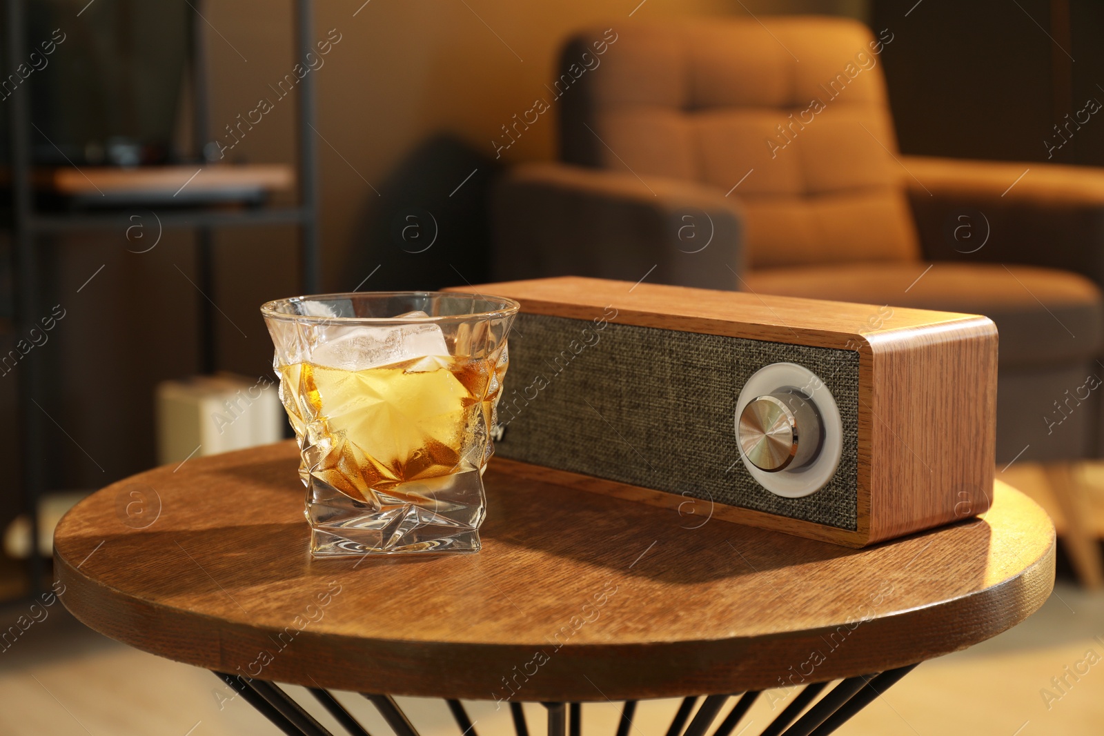 Photo of Glass of whiskey and portable speaker on wooden table in room. Relax at home