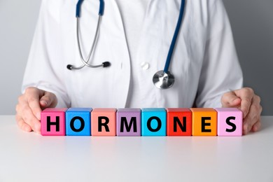 Doctor near word HORMONES made with colorful cubes at white table, closeup