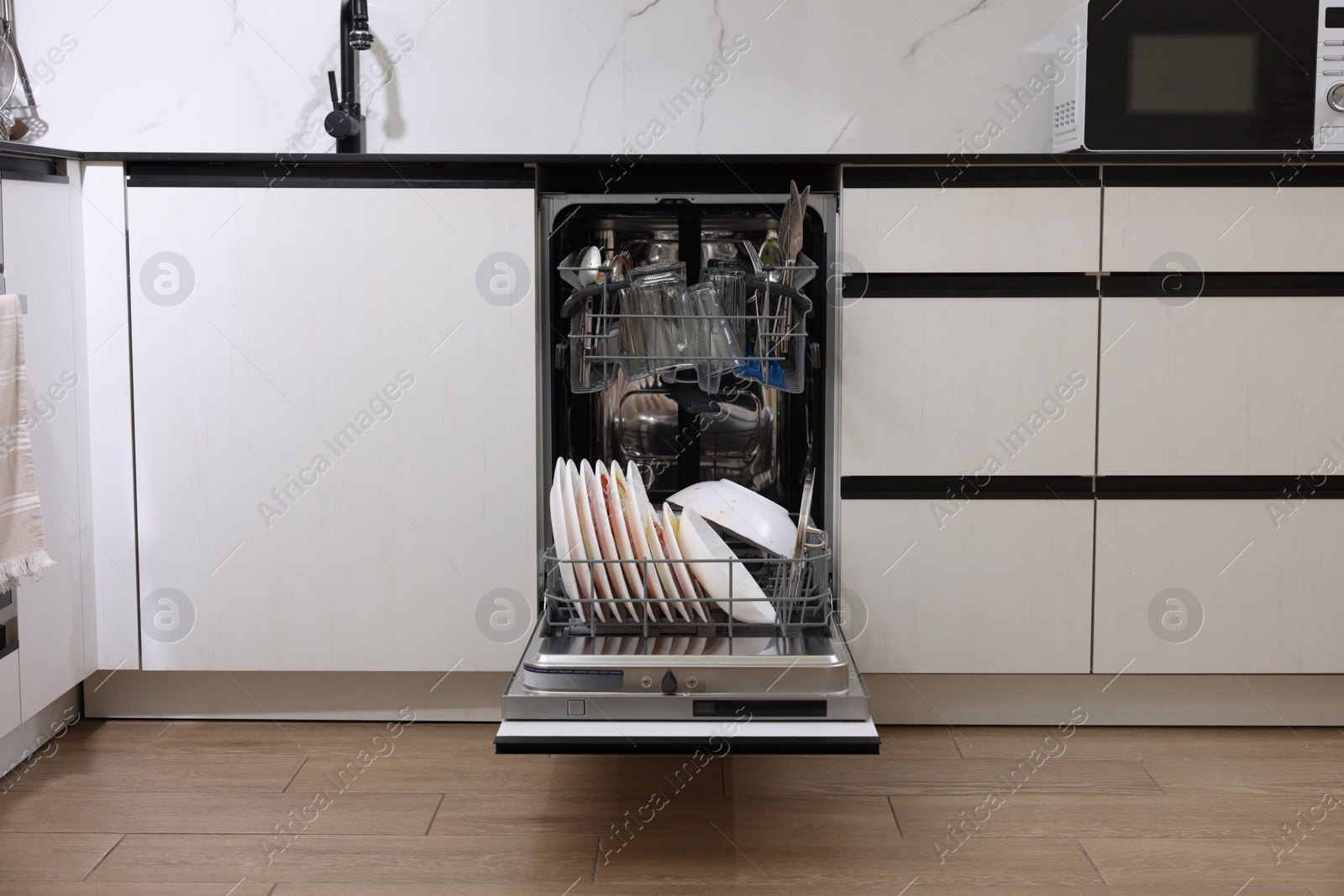 Photo of Open modern dishwasher with dirty tableware in kitchen