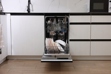 Photo of Open modern dishwasher with dirty tableware in kitchen