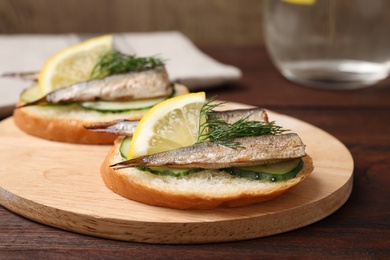 Delicious sandwich with sprats, cucumbers, lemon and dill on wooden board, closeup