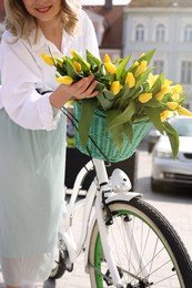 Photo of Woman with bouquet of yellow tulips and bicycle on city street, closeup