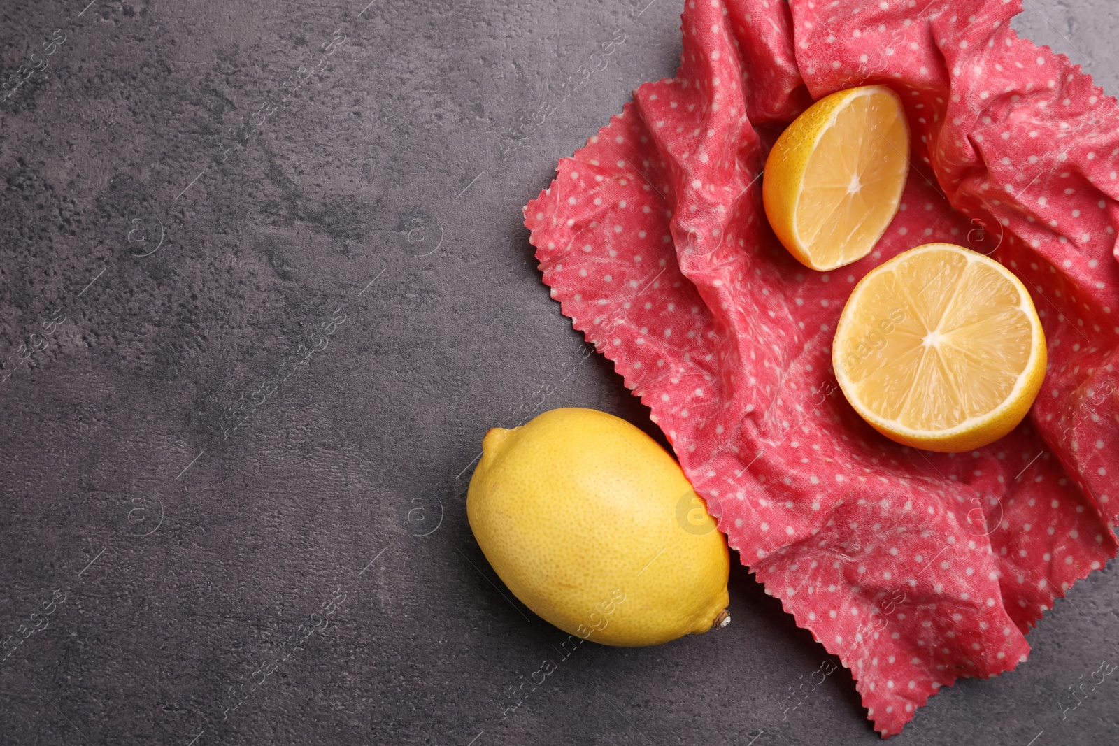 Photo of Whole and cut fresh lemons with beeswax food wrap on grey table, flat lay. Space for text