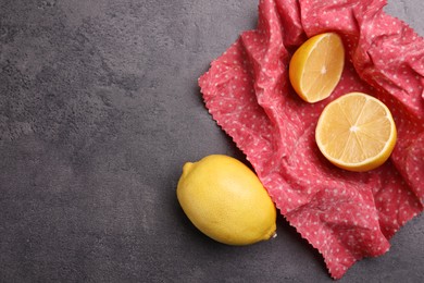 Photo of Whole and cut fresh lemons with beeswax food wrap on grey table, flat lay. Space for text