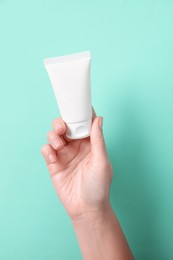 Photo of Woman with tube of hand cream on turquoise background, closeup