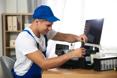 Photo of Repairman with screwdriver fixing modern printer in office