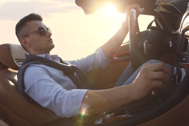 Businessman driving luxury convertible car outdoors on sunny day