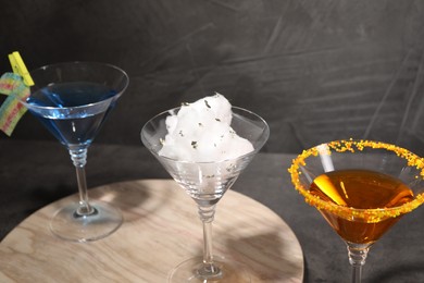 Photo of Tasty cotton candy cocktail and other alcoholic drinks in glasses on table against gray textured background