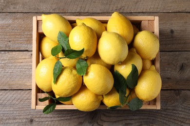 Photo of Fresh lemons and green leaves in crate on wooden table, top view