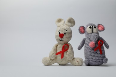 Cute knitted toys with red ribbons on light grey background, space for text. AIDS disease awareness