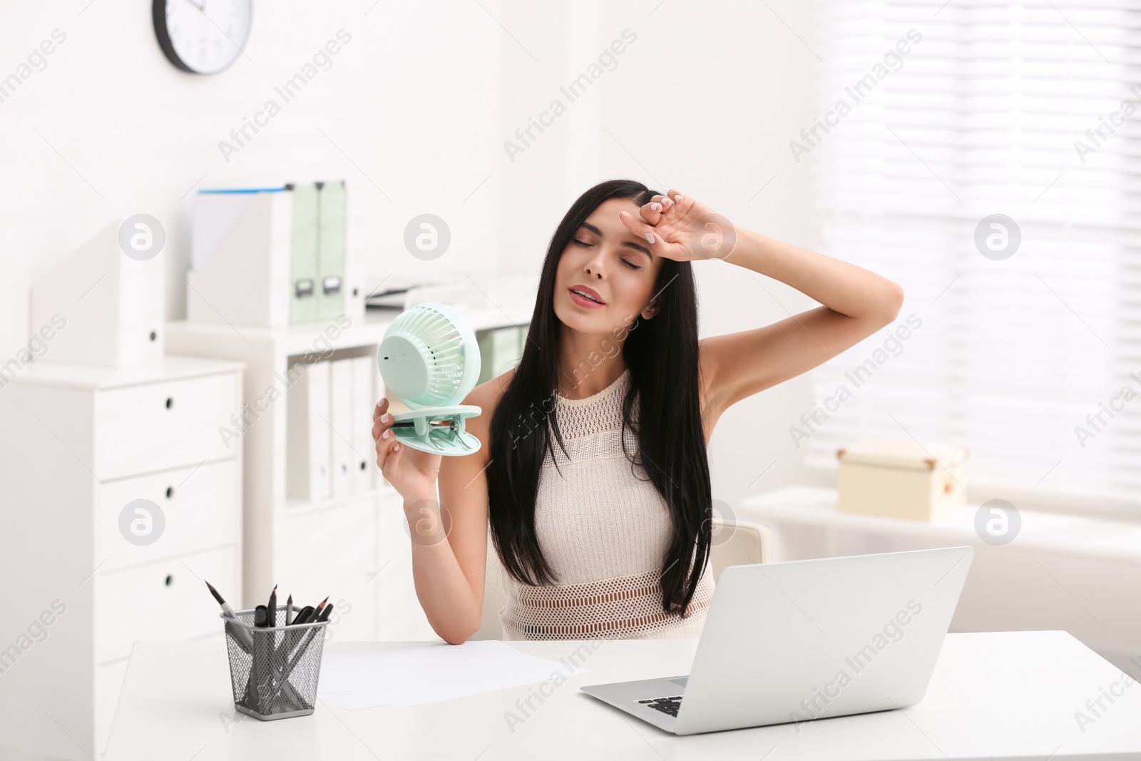 Photo of Young woman enjoying air flow from fan at workplace