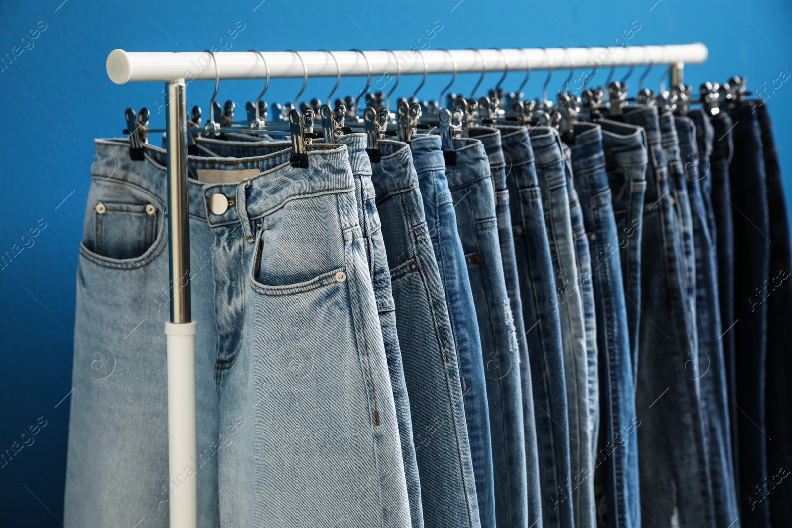 Photo of Rack with stylish jeans on blue background, closeup