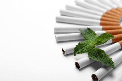Photo of Menthol cigarettes and fresh mint leaves on white background. Space for text
