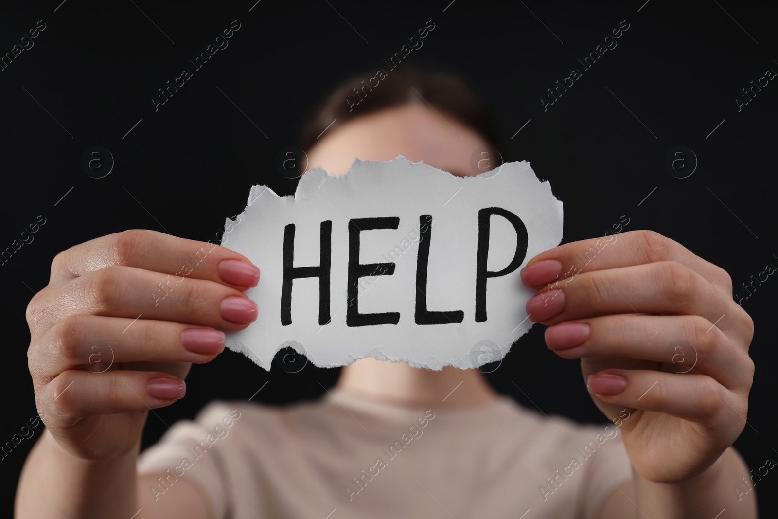 Photo of Woman holding piece of paper with word Help on black background, closeup. Domestic violence concept