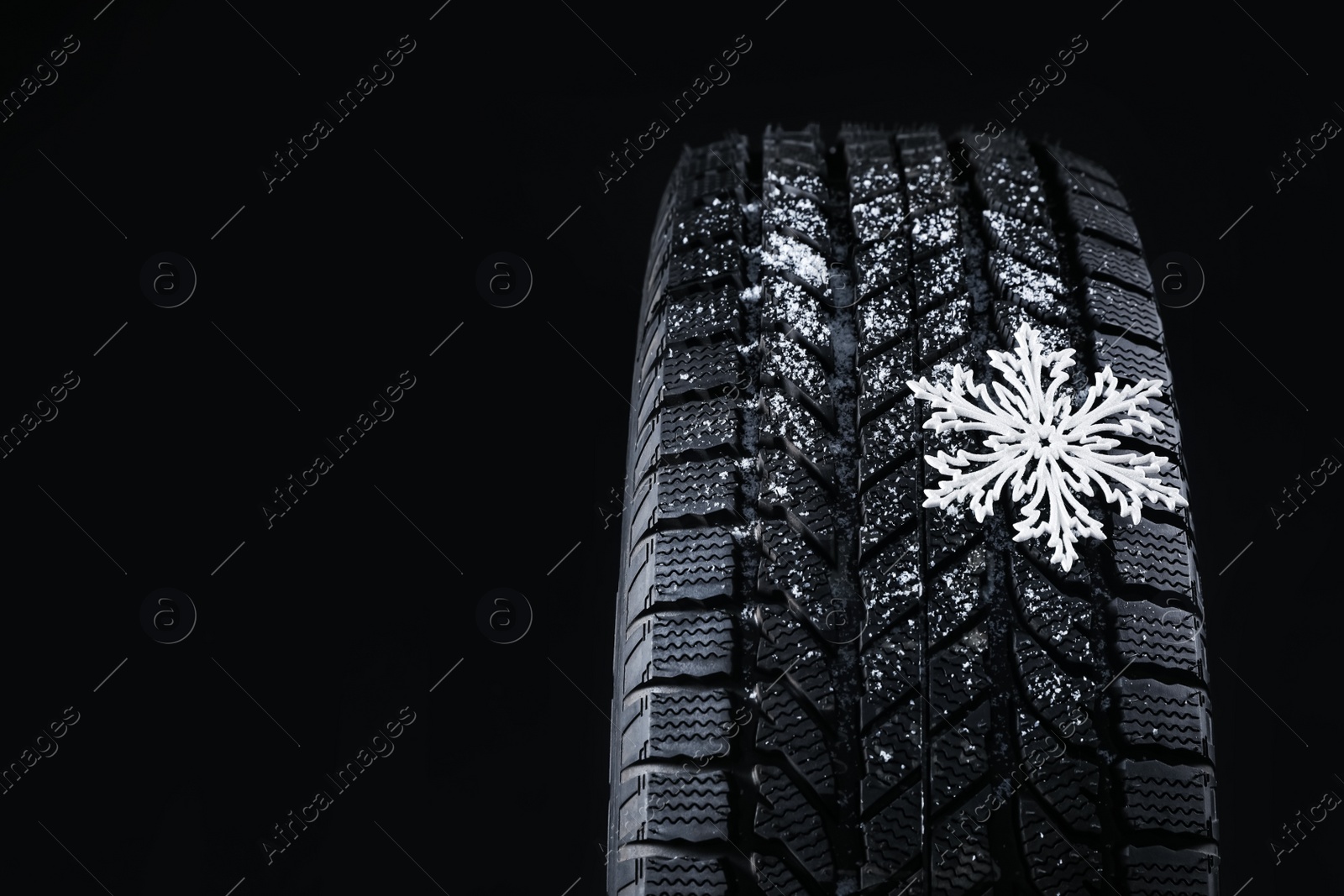 Photo of Winter tire with decorative snowflake on black background, closeup. Space for text