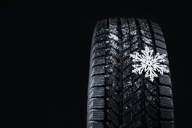 Photo of Winter tire with decorative snowflake on black background, closeup. Space for text