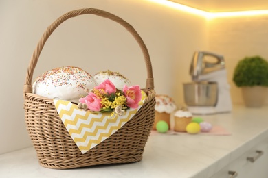 Photo of Traditional Easter cakes and flowers in basket on kitchen counter, space for text