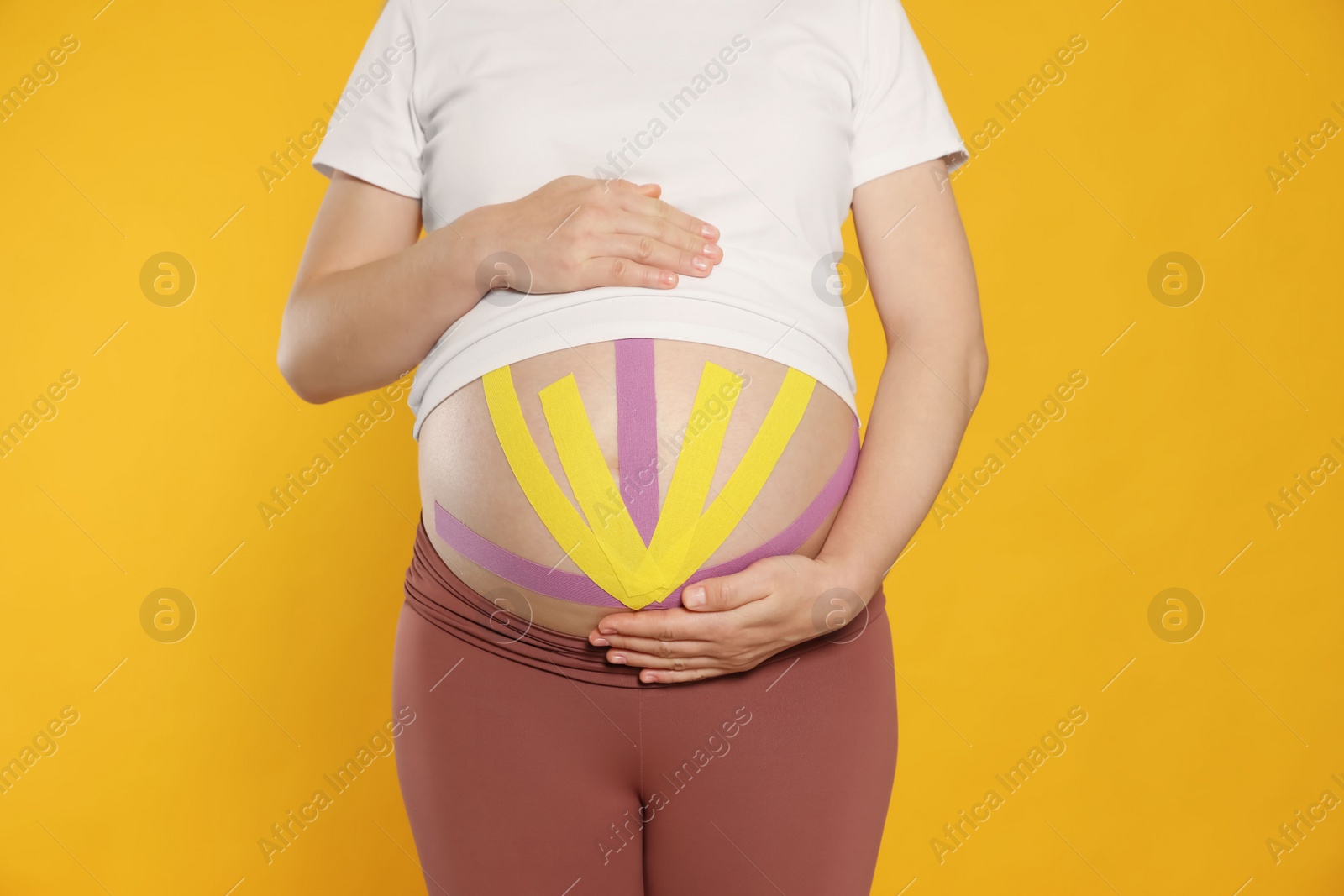 Photo of Pregnant woman with kinesio tapes on her belly against orange background, closeup