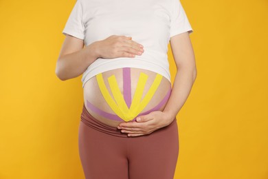 Pregnant woman with kinesio tapes on her belly against orange background, closeup