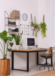 Cozy workplace with computer, modern furniture and houseplants at home