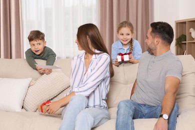 Photo of Cute little children presenting their parents with gifts on sofa at home