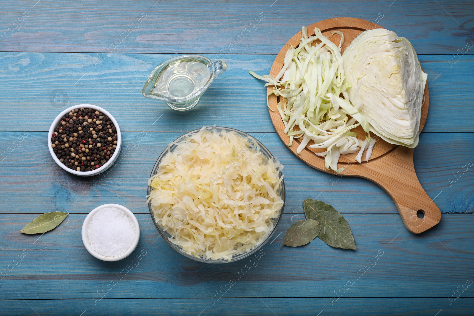 Photo of Bowl of tasty sauerkraut and ingredients on light blue wooden table, flat lay