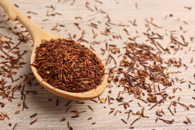 Spoon with dry rooibos leaves on wooden table, closeup. Space for text