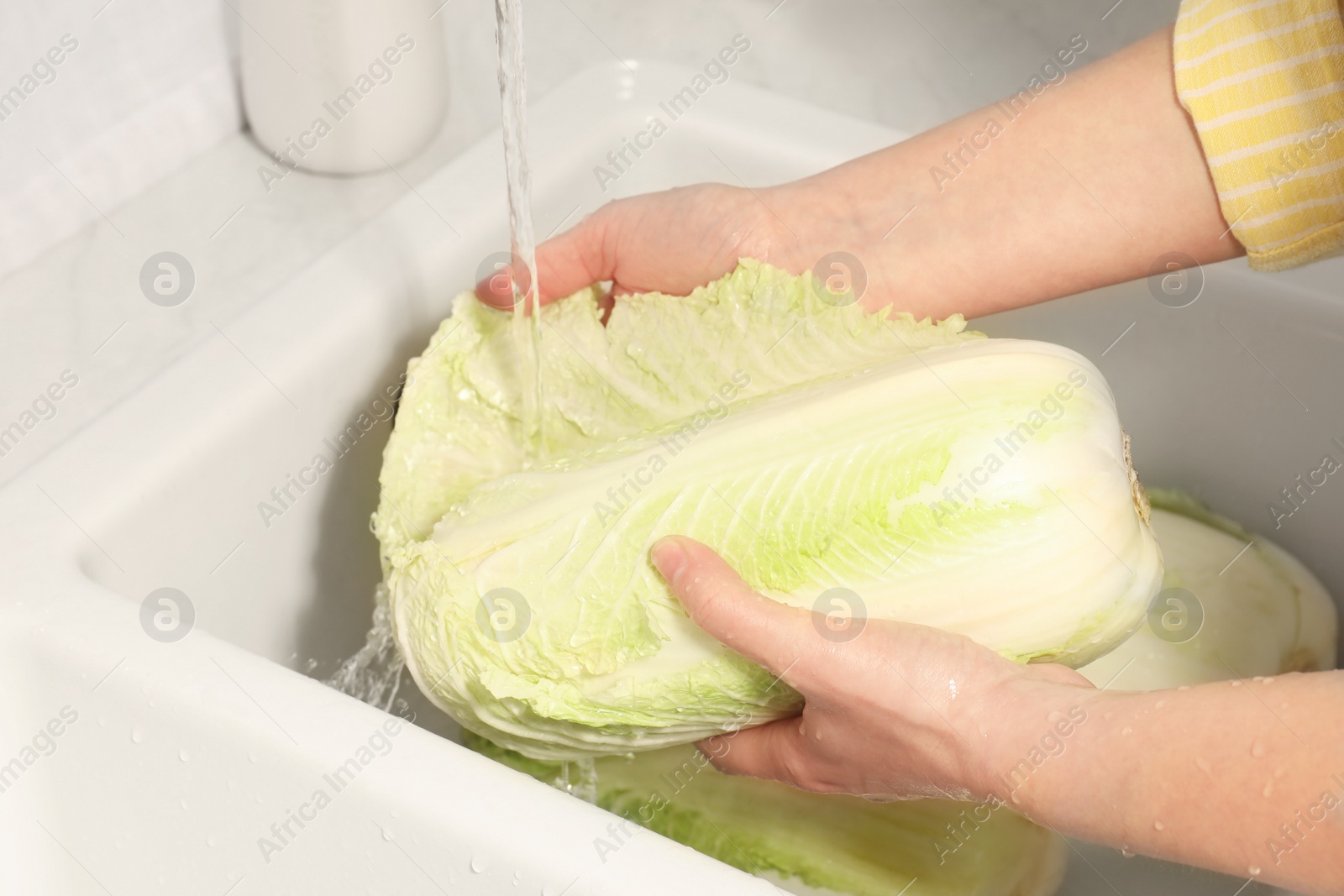 Photo of Woman washing fresh chinese cabbage under tap water in kitchen sink, closeup