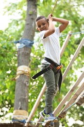 Little African-American boy climbing in adventure park. Summer camp