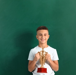 Photo of Happy boy with golden winning cup on near chalkboard